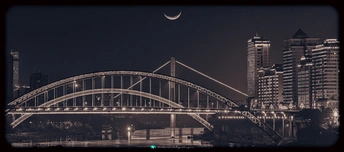 夜晚跨河大桥的照片 背景中有月亮和建筑物