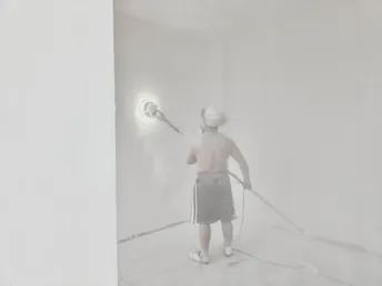 一个拿着水管的男子在白色的房间里向地板上喷水