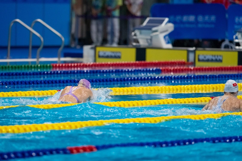 一个在游泳池里游泳的人 水中有其他人。