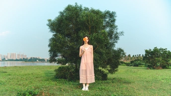 一位穿着粉红色连衣裙 手持雨伞站在绿色草地上的一名女子