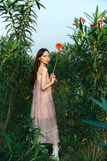 一位穿着粉红色连衣裙的年轻女子手里拿着一朵花站在花园里