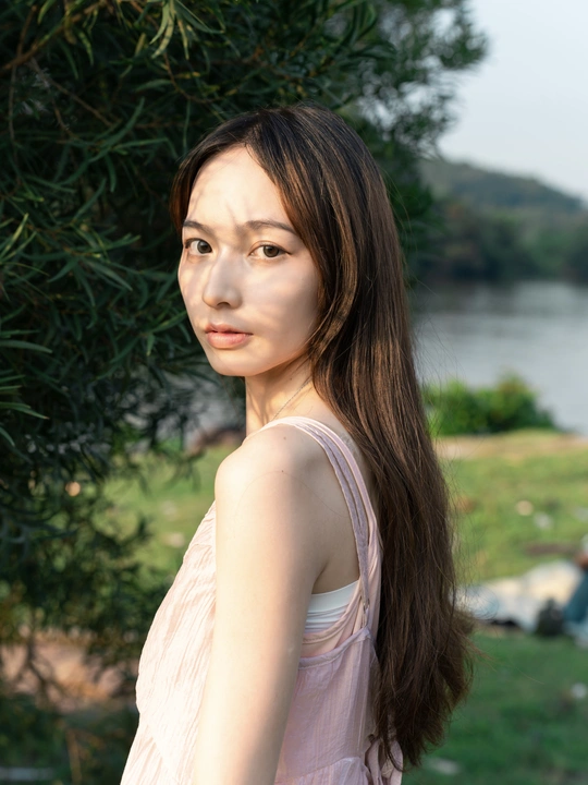 一位穿着粉红色裙子的年轻女子在靠近水域的地方为相机摆姿势