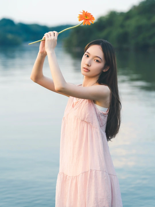 粉色连衣裙的年轻美女手持花站在水边