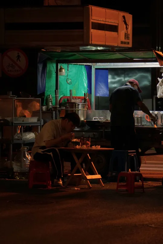 一个男子站在一张桌子旁 而夜晚餐厅外面的人们都坐着。