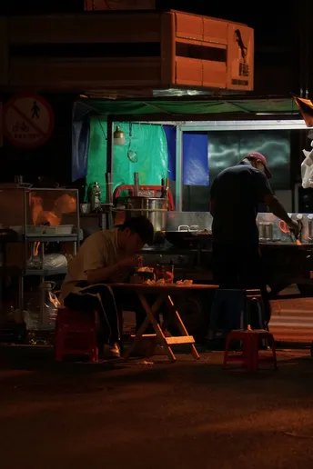 一个男子站在一张桌子旁 而夜晚餐厅外面的人们都坐着。