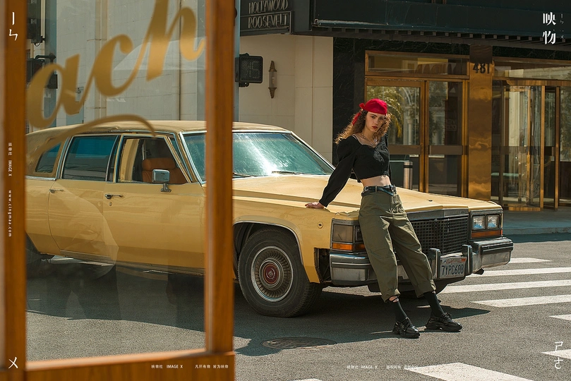 一位年轻女子站在一条街道上 前面是一辆旧黄色的汽车。