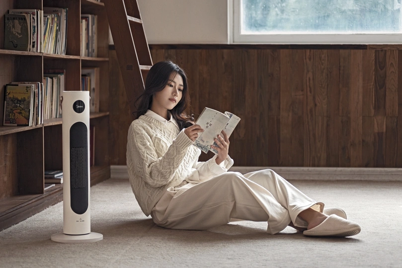 一个年轻女子坐在地板上 手里拿着一杯茶在读一本书。