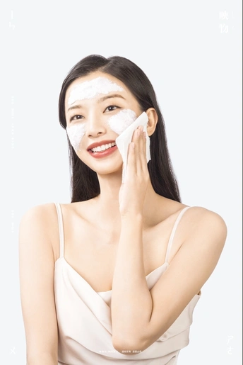 一个美丽的年轻女子身上披着一条白色的毛巾 脸上敷着奶白色的面霜。