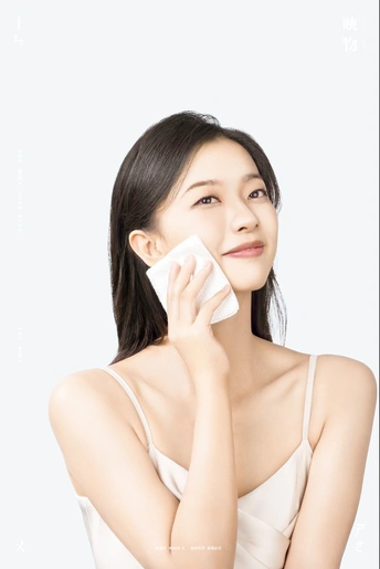 一位年轻女子正在用一块白毛巾擦拭她的脸。