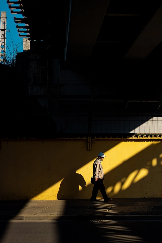 一个人走在一条有黄色墙壁和建筑阴影的街道上