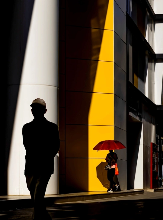 一个人和一个女人 带着红伞 走在靠近高楼的一条街道上。