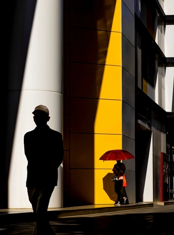 一个人和一个女人 带着红伞 走在靠近高楼的一条街道上。