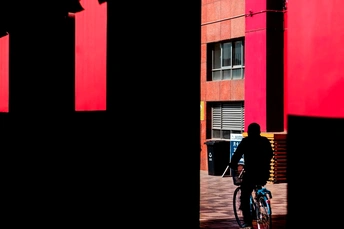 一个人骑自行车沿着一座有红墙的高楼旁的街道