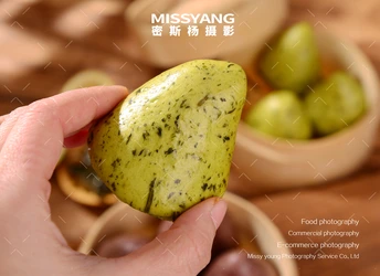 一只手拿着一个绿色的梨放在一碗水果旁边