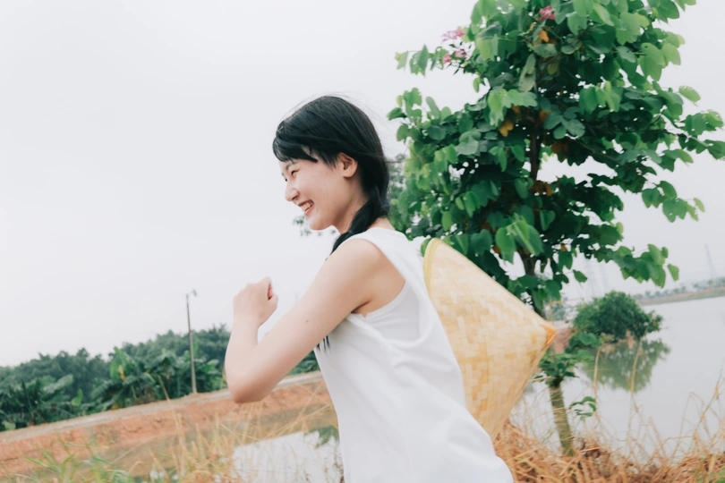 一位身穿白色连衣裙的年轻女子撑着伞站在水边的田地里