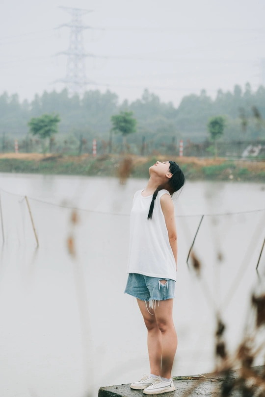 一个打着白伞的年轻女子站在桥上 在雨中眺望湖面
