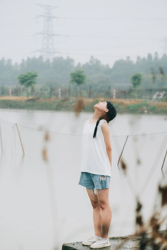 一个打着白伞的年轻女子站在桥上 在雨中眺望湖面