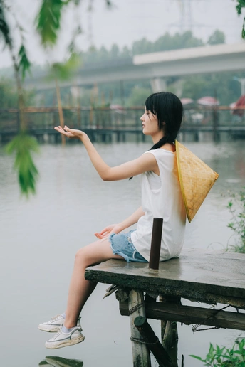 一个年轻的女人撑着伞坐在木码头上俯瞰着一条河