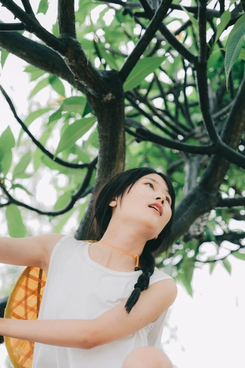 一个穿着白色连衣裙的年轻女子把手举到树上