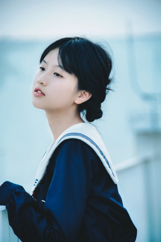 一位身穿黑白校服的年轻女子站在白墙前