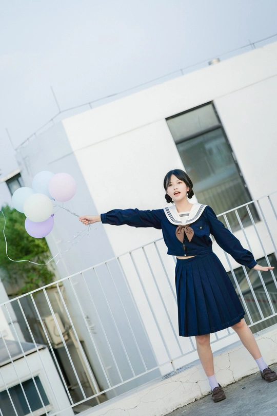 一位身穿蓝色连衣裙、手持气球的年轻女子站在一栋大楼前