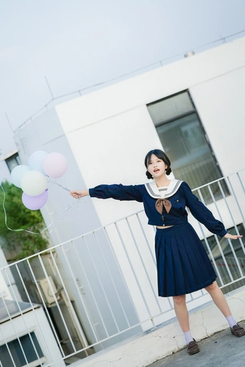 一位身穿蓝色连衣裙、手持气球的年轻女子站在一栋大楼前