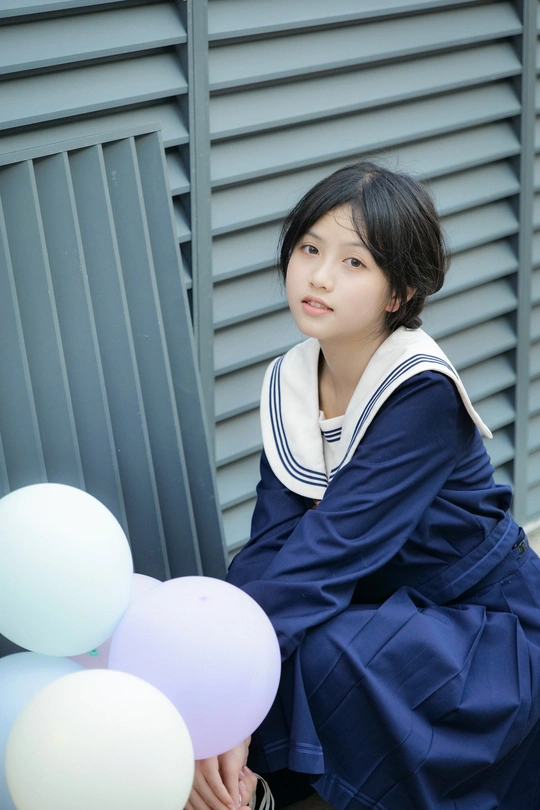 一名身穿校服的年轻女子在一栋带着白色气球的大楼前摆姿势