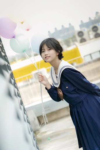 一名身穿校服、手持气球和雨伞的年轻女子站在一栋大楼前