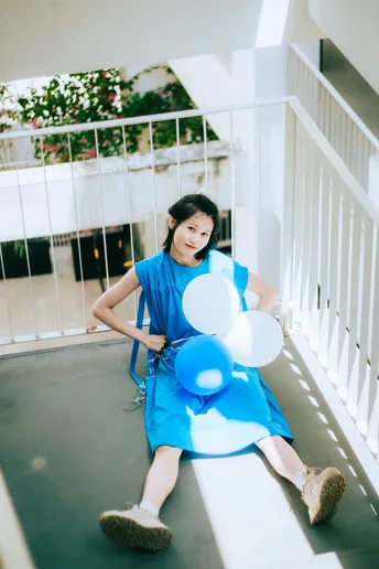 一个穿着蓝色连衣裙的年轻女子坐在楼梯上抱着气球