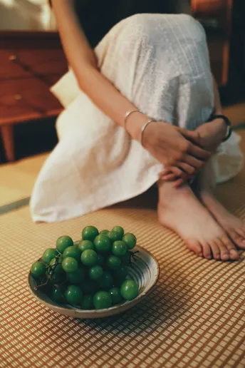 一个女性坐在桌子旁 她的脚放在一盘绿葡萄上
