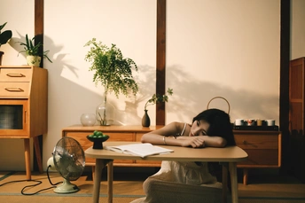 一个年轻女子将头靠在带有书桌和盆栽的房间地板上