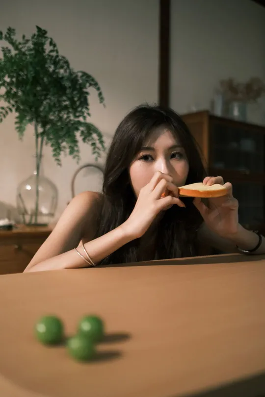 一个年轻女子坐在桌子旁 手里拿着一块披萨 嘴里含着一个绿色饼干。