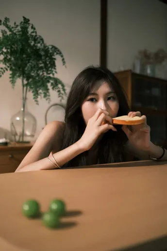 一个年轻女子坐在桌子旁 手里拿着一块披萨 嘴里含着一个绿色饼干。