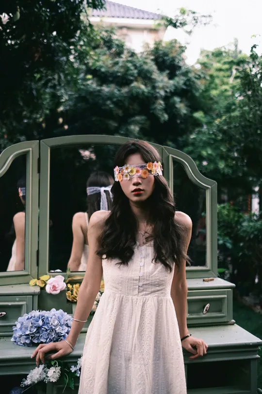 一位戴眼镜的年轻女子穿着白色连衣裙站在镜子前