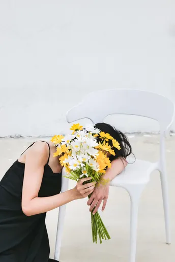 一位穿着黑色连衣裙 手持一束黄白相间的花束的女士