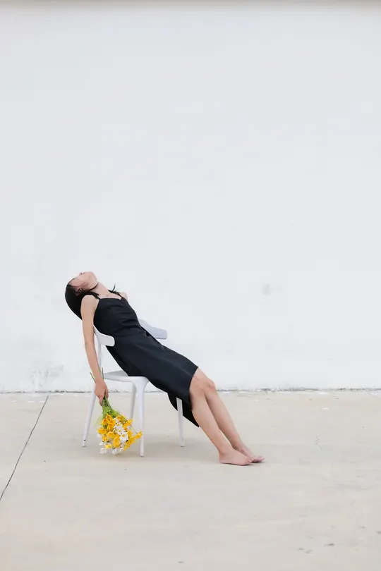 一个穿黑色连衣裙的女人坐在带有黄色花朵的白色椅子上
