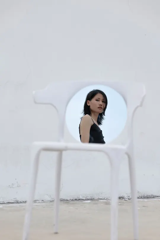 一个穿黑色衣服的年轻女子坐在白色椅子上 照镜子