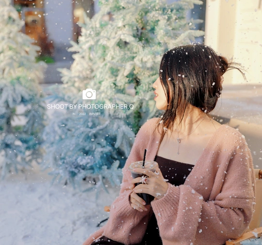 一个年轻的女人坐在雪地里的圣诞树前