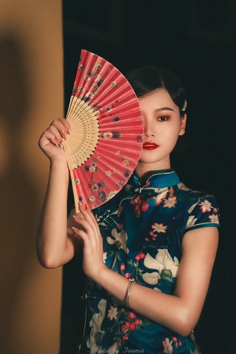 一位身穿碎花连衣裙、手里拿着红色雨伞的年轻女子站在黑色背景前