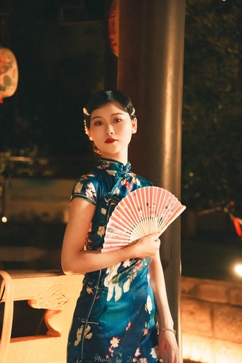 一位身穿蓝色连衣裙、手持扇子和雨伞的年轻女子站在外面