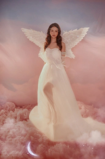 一个美丽的女人打扮成天使 长着白色的翅膀 站在粉红色的云上