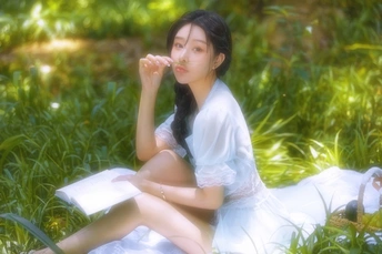 一个穿着白色连衣裙的年轻女子坐在草地上