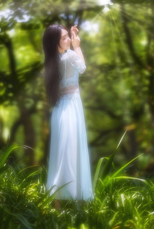 一位身穿白色连衣裙、留着长发的年轻女子站在树林里的照片
