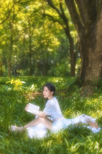 一个穿着白色连衣裙的年轻女子坐在树林里的草地上看书