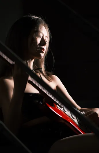 一个年轻女子坐在光线昏暗的房间里弹吉他