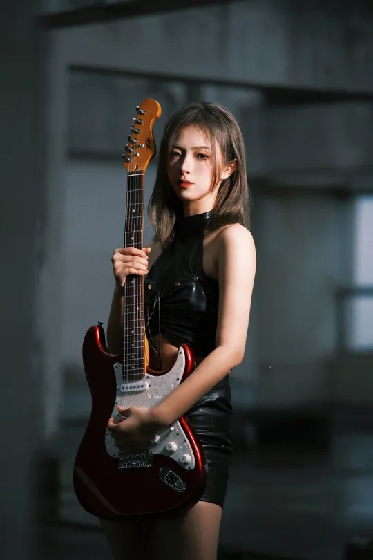 一位年轻女子正在弹奏一把红黑色的吉他