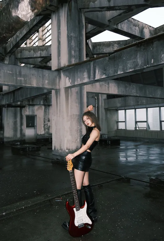 一个年轻女子站在一座废弃的建筑中 手里拿着一把吉他。