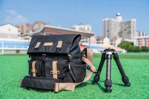 一个背包里装着三脚架和一台相机在绿色的草地上