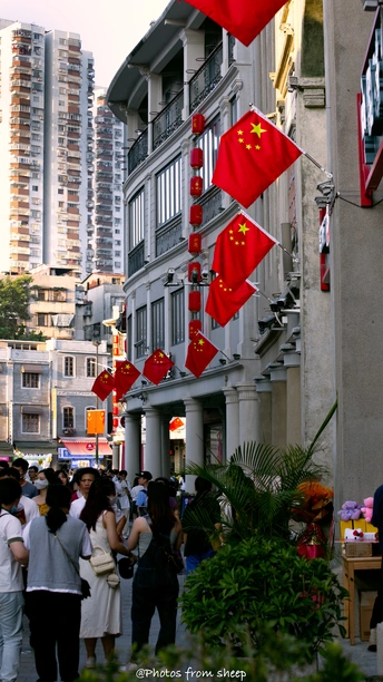 许多人走在建筑物上挂着红旗的街道上