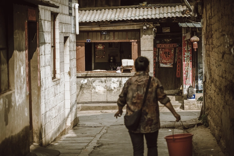 一位女士提着一只桶穿过一座城市的老式建筑之间的狭窄小巷。